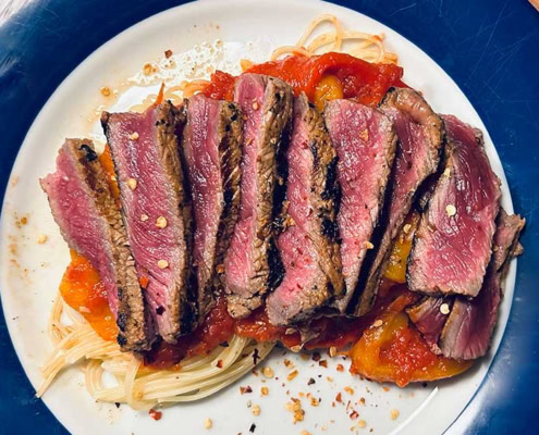 Saftiges Rindersteak auf Pasta mit Tomatensauce und Gewürzen.