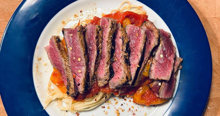 Saftiges Rindersteak auf Pasta mit Tomatensauce und Gewürzen.